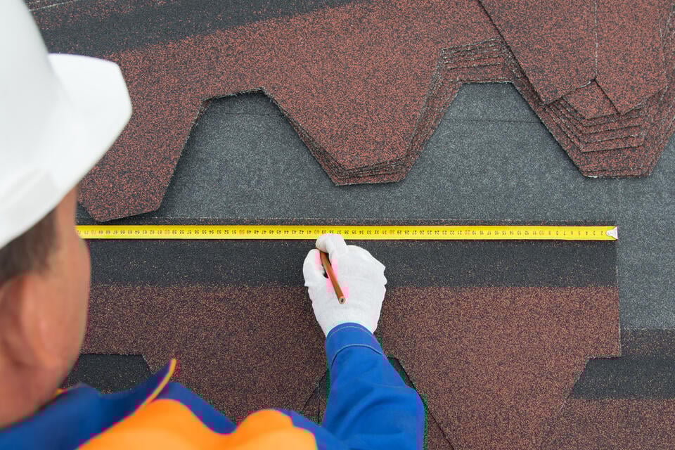 how to measure a roof for shingles-over the shoulder view of man measuring roof shingles