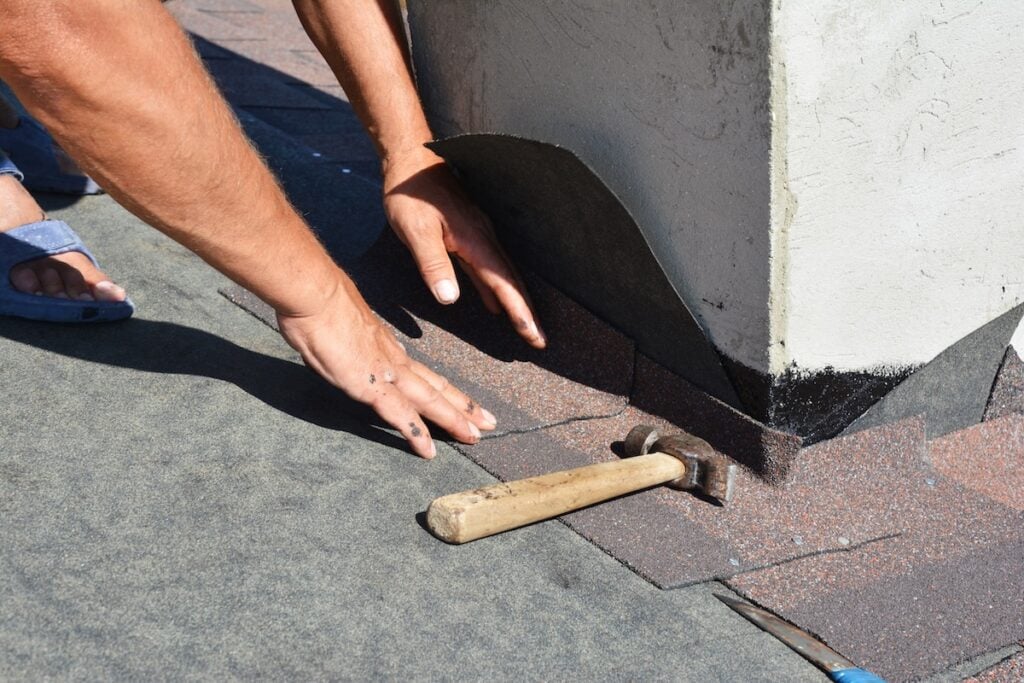 Roofer laying asphalt shingles around base of chimney as flashing