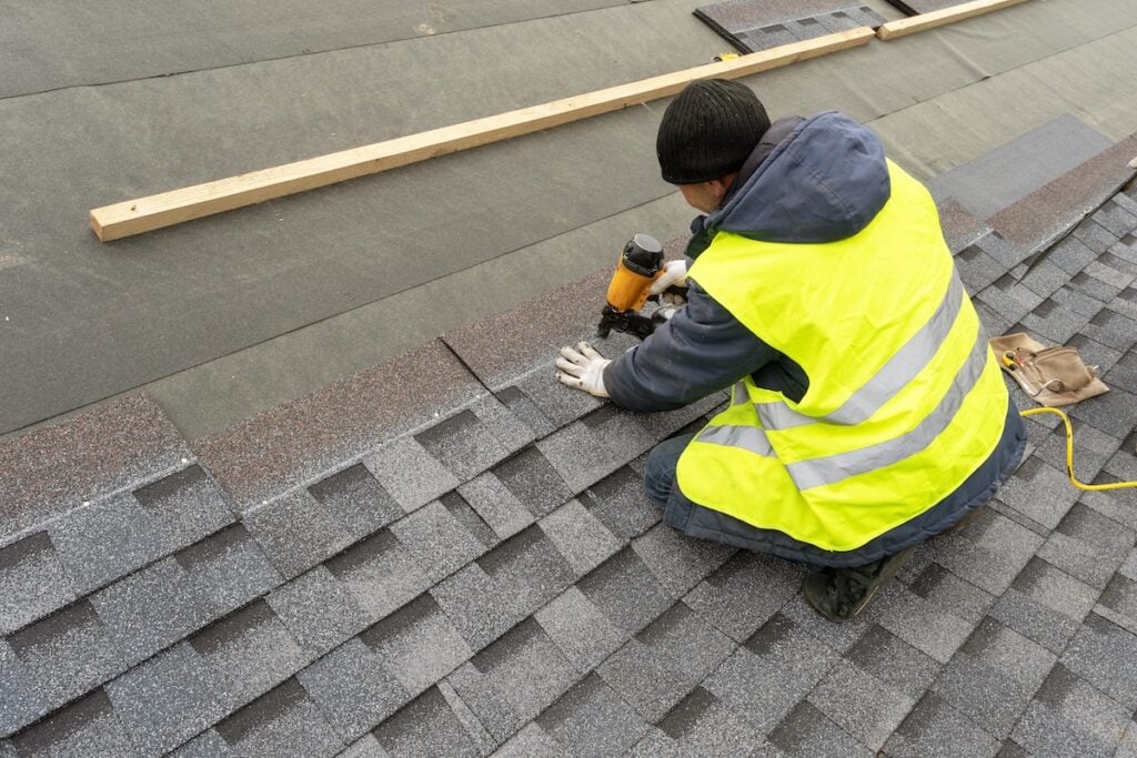A roofer installing gray asphalt shingles on residential home